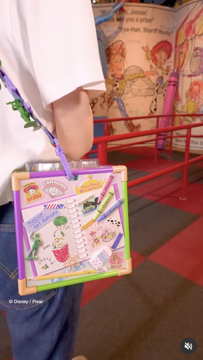 Person with a Toy Story-themed Etch A Sketch bag stands in a colorful Tokyo Disneyland amusement park queue.